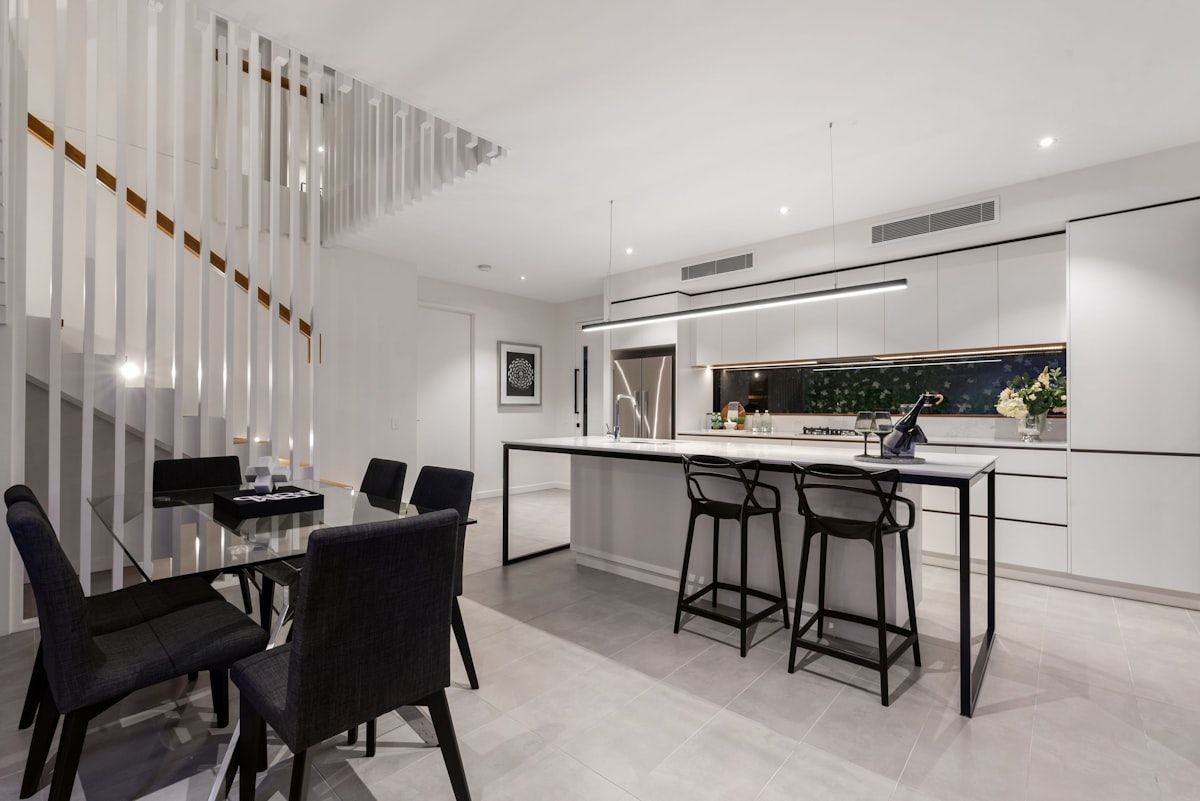 A modern Brisbane home interior with an unfinished stair opening, showing a straight timber staircase in one area and a more elaborate feature staircase with steel stringers, timber treads and a glass balustrade in another, emphasizing the contrast between a simpler and a premium custom build.