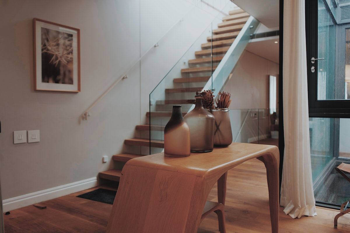A finished custom staircase in a modern home, combining timber treads, a glass balustrade, slim metal handrails, and integrated LED strip lighting under the treads, with daylight coming through nearby windows and the stair risers clearly visible for safe walking