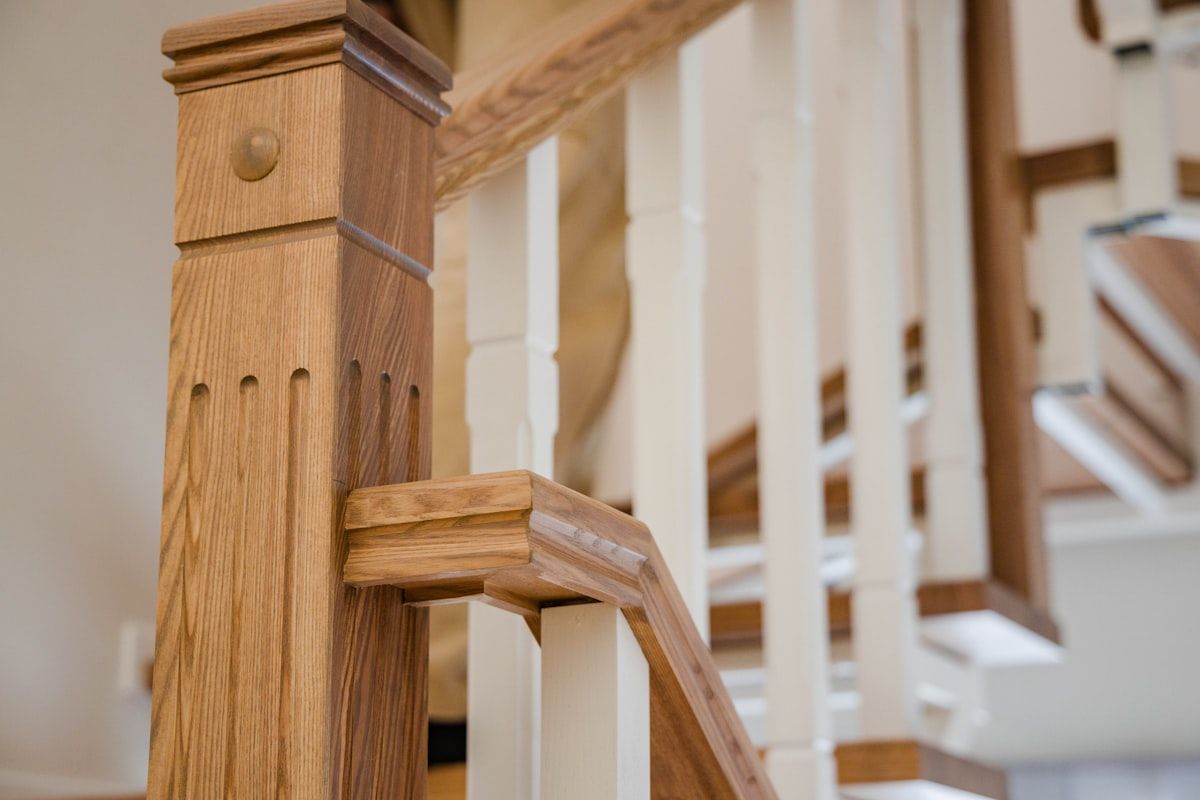 A close interior view of a timber staircase showing several stair treads in different wood tones, including light oak, blackbutt, spotted gum and a darker hardwood sample, with a handrail and open-riser section highlighting the grain, finish and color variation.